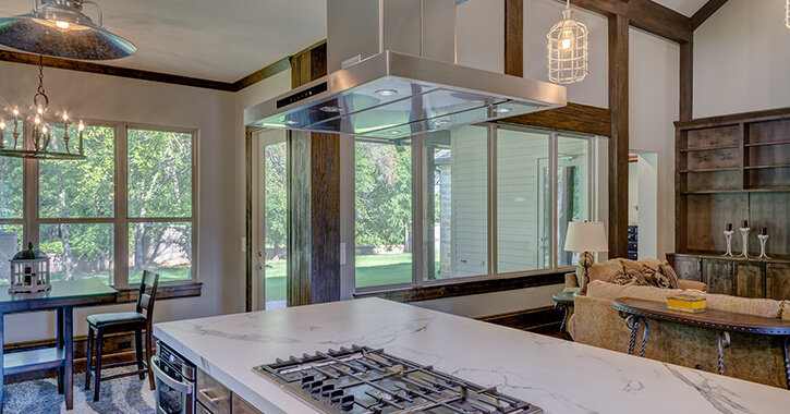 Large kitchen with marble-topped island, large hood above stove, and big windows looking out onto backyard.